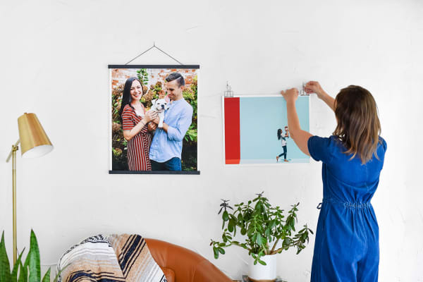 A woman hangs two Fine Art Photo Prints with black poster rails and silver skeleton clips.