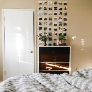 A grid of fifty-four Square Prints are hung in a neat grid above a dresser in a bedroom.