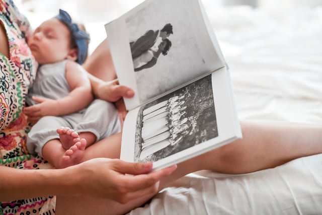 A parent holds a sleeping baby and an open 8x8 Hardcover Photo Book A parent holds a sleeping baby and an open 8x8 Hardcover Photo Book