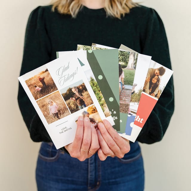 A woman holds a fanned set of flat holiday photo cards with family photos and greetings.