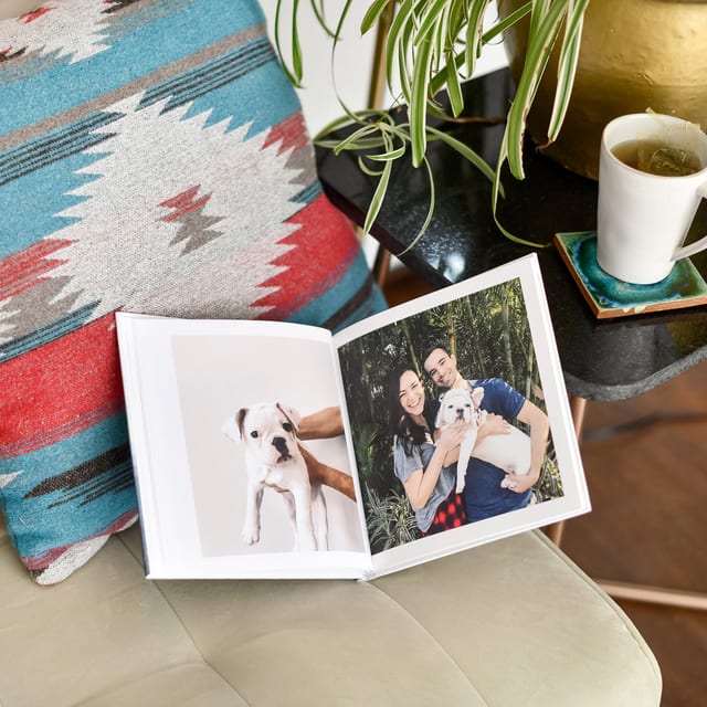 An open Hardcover Photo Book on a couch, a puppy portrait on the left and a couple with the puppy on the right An open Hardcover Photo Book on a couch, a puppy portrait on the left and a couple with the puppy on the right