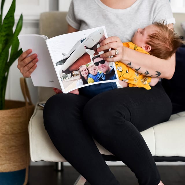 A parent holds a sleeping baby and looks through an open 8x8 Softcover Photo Book A parent holds a sleeping baby and looks through an open 8x8 Softcover Photo Book