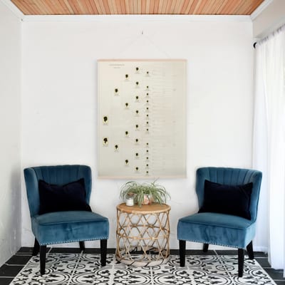 A MyCanvas Family Tree poster hangs in a wooden rail frame above a rattan side table, flanked by two teal velvet armchairs.