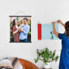Two Fine Art Prints are hung above a big comfy chair. The first hangs from Black Poster Rails, and the second is being hung from Skeleton Clips by a woman in a blue dress.