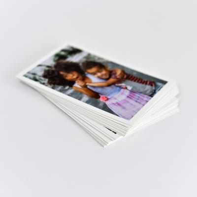 A stack of Classic Prints with white borders. The top print shows two children hugging eachother. A stack of Classic Prints with white borders. The top print shows two children hugging eachother.