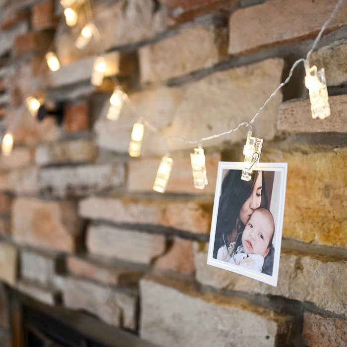 A single Gold Foil bordered Square Print hangs against a fireplace from a set of Clip Lights.