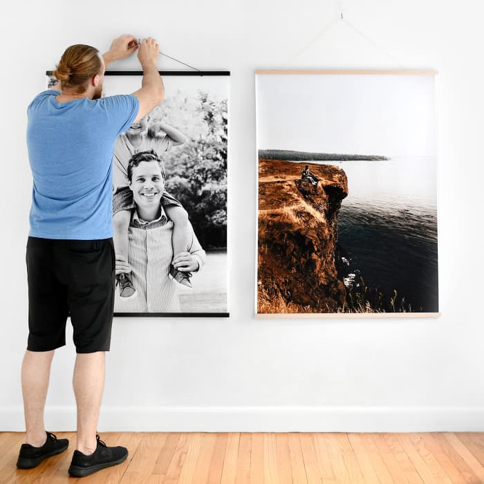 A person hangs an Engineer Print from 36 inch Black Wood Rails next to another Engineer Print in Maple Rails.