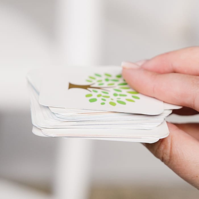 A hand holds a thick stack of MyCanvas Family Flip memory game cards, the top showing the tree-illustrated back.