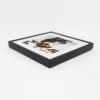 A single black framed photo print lays flat on its back to showcase the corner detail of the frame.