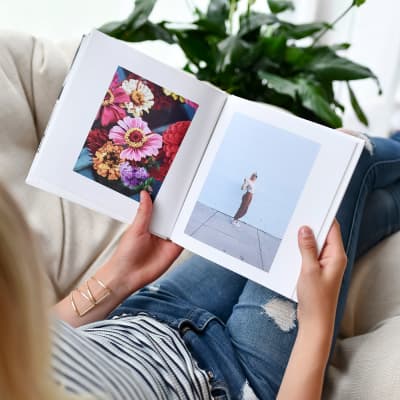 A person sits in on a beige chair and pages through an 8 inch Hardcover Photo Book.