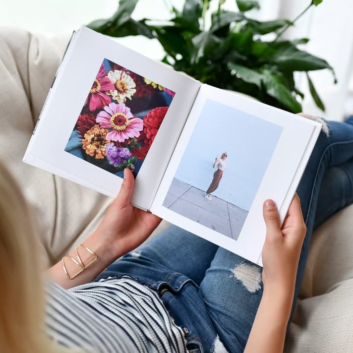 A person sits in on a beige chair and pages through an 8 inch Hardcover Photo Book.