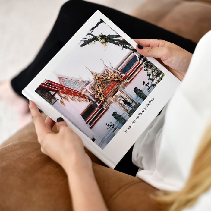 A person sits on a suede couch and holds a Hardcover Photo Book of vacation photos in their hands.