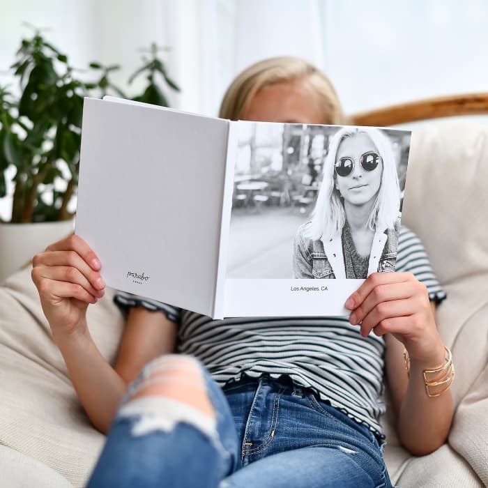 A girl looks at a Hardcover Photo Book titled, Los Angeles, California, with a Black and White portrait on the cover.