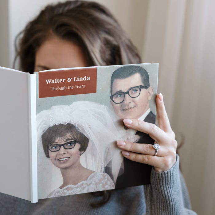 A woman holds open a MyCanvas Hardcover Photo Book titled Walter & Linda Through the Years, showing a vintage wedding portrait of a bride and groom.