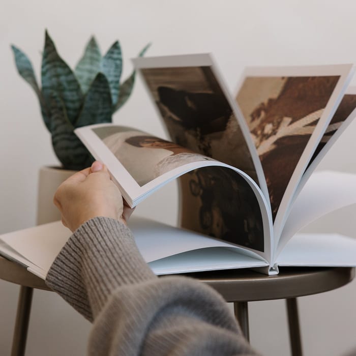 A hand fans through the pages of a MyCanvas Hardcover Photo Book filled with vintage family photos, with a snake plant in the background.