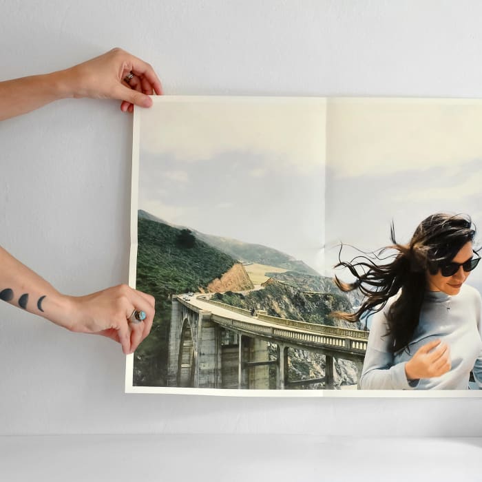 Hands hold a Newsprint of a traveler on a bridge. The Newsprint has crisp creases from being folded in fourths.