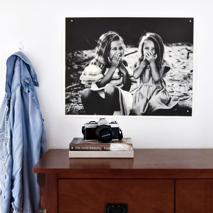 A black and white Newsprint of a photo of two children laughing hangs from Good Hangups above a dresser.