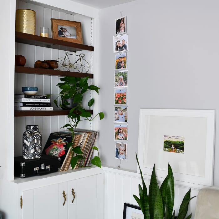 A column of photo prints showing fun family photos on a Vertical Photo Rope hang next to a bookshelf.