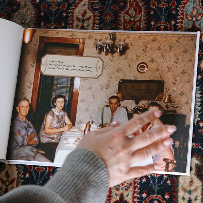 A MyCanvas Premium Hardcover Photo Book lies open to a captioned vintage color photo of a family gathered around a dining table.