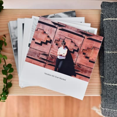 A stack of 8 inch Softcover Photo Books is fanned out on a table. The top book cover shows a fun vacation.