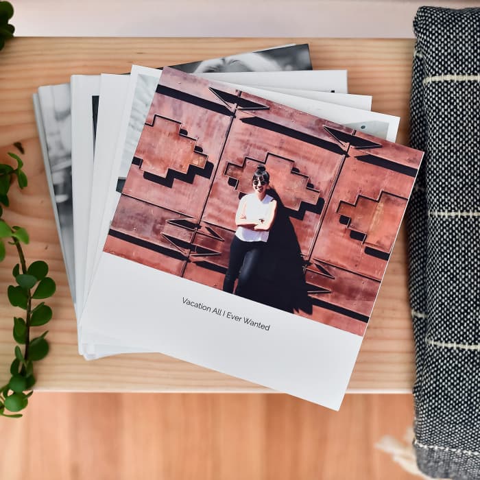 A stack of 8 inch Softcover Photo Books is fanned out on a table. The top book cover shows a fun vacation.