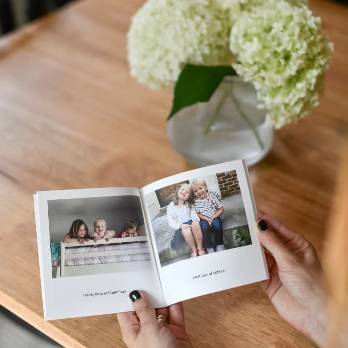 Two hands page through a 6 inch Softcover Photo Book of memories, showing cute photos of children.