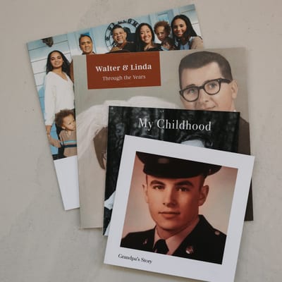 A fanned stack of four MyCanvas Softcover Photo Books, with covers titled Walter & Linda Through the Years, My Childhood, and Grandpa's Story.