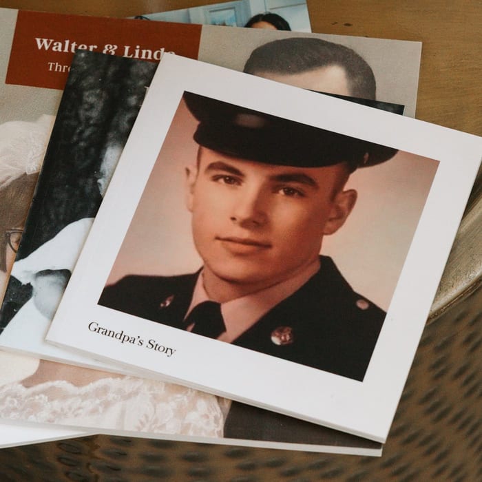 A MyCanvas Softcover Photo Book titled Grandpa's Story sits on a wicker stool, its cover showing a vintage portrait of a young man in military uniform.