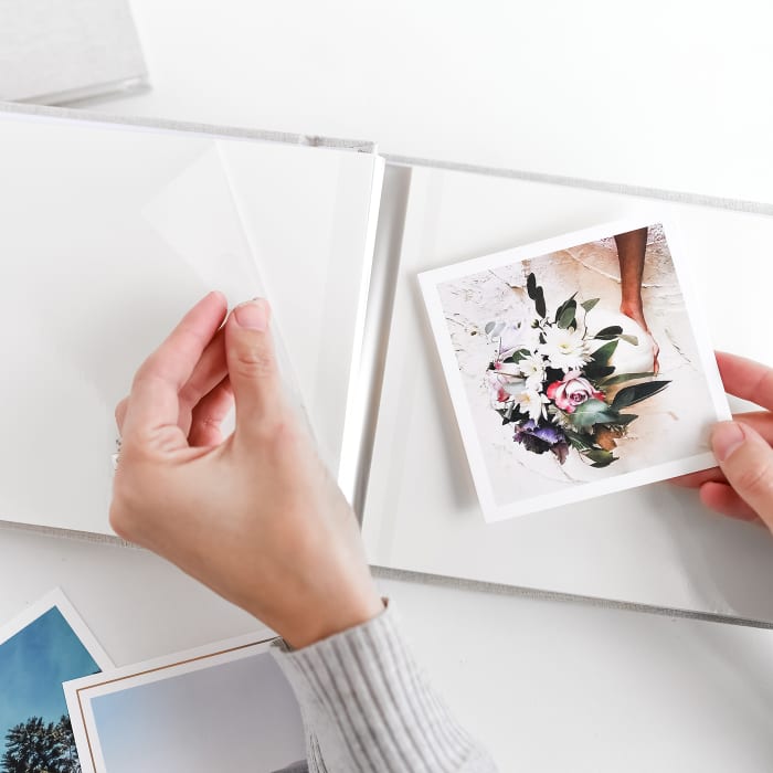 Two hands lift a plastic page cover to place a Square Print into a photo album.