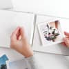 Two hands lift a plastic page cover to place a Square Print into a photo album.