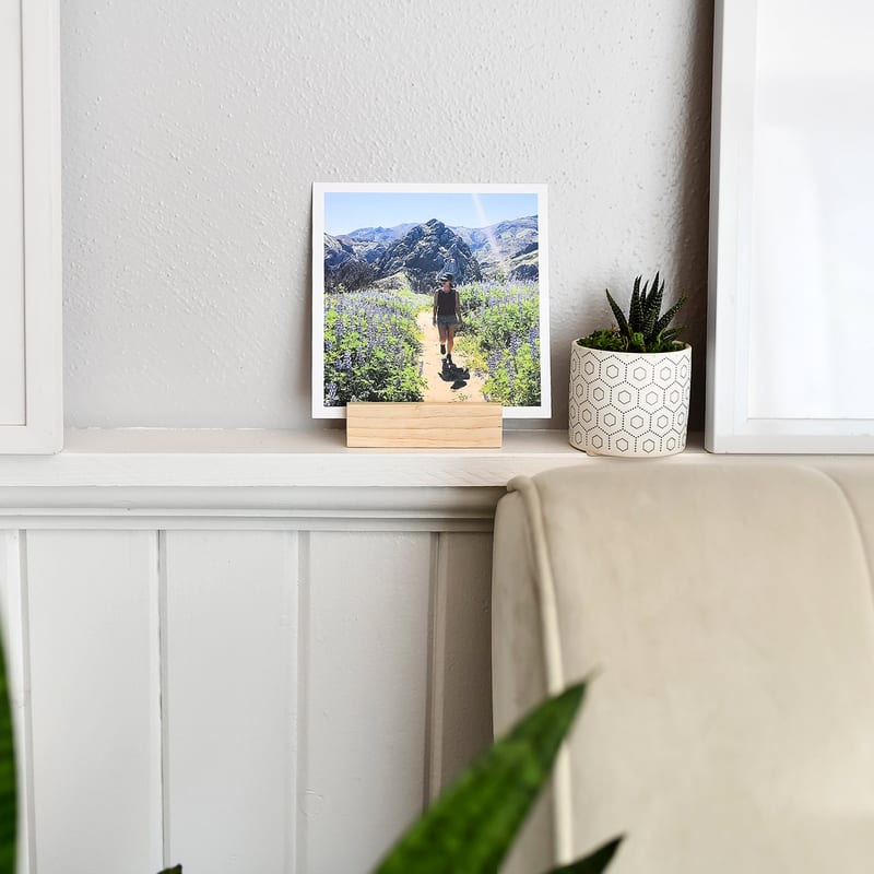 A square photo print of a mountain trail in a wooden photo block on a ledge.