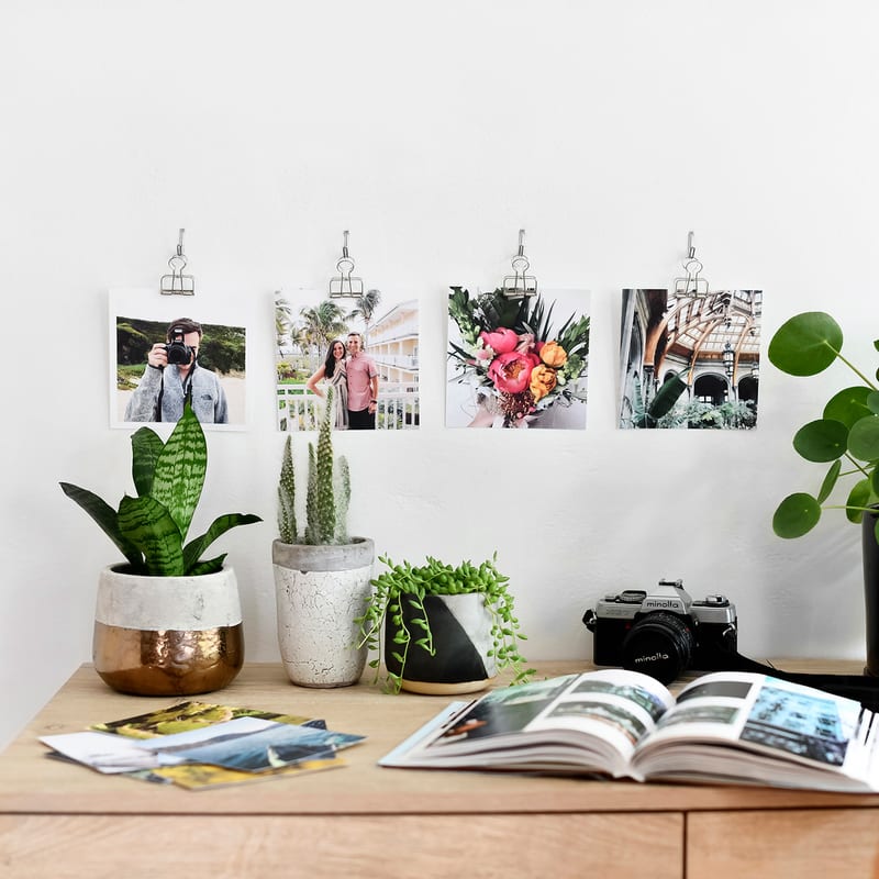 Four square photo prints clipped above a desk.