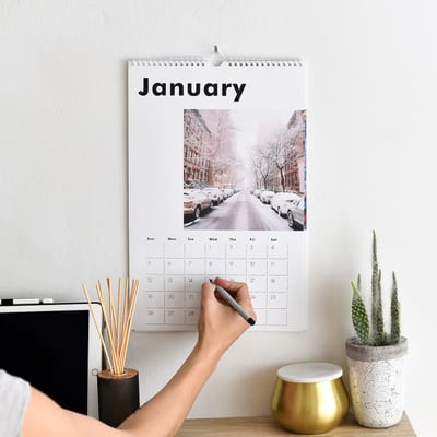 A person makes a note on the Large Wall Calendar hanging above their desk.
