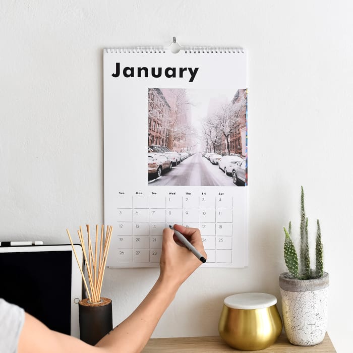A person makes a note on the Large Wall Calendar hanging above their desk.